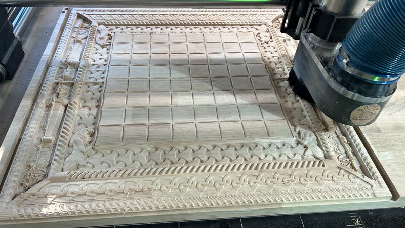 Ornate wooden board with a carved lattice border being cut on the CNC bed