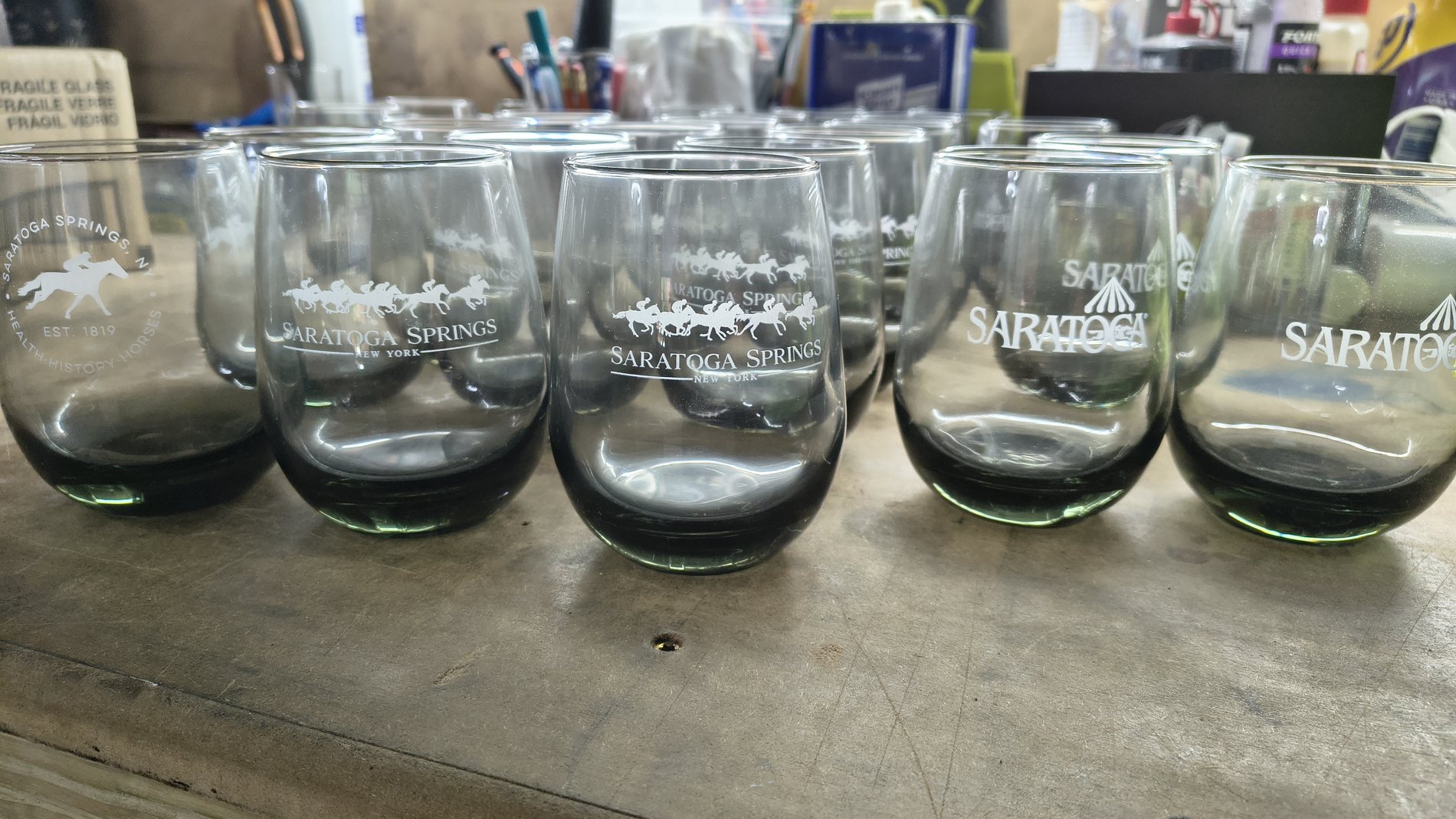 Row of etched glass tumblers arranged on a workshop counter