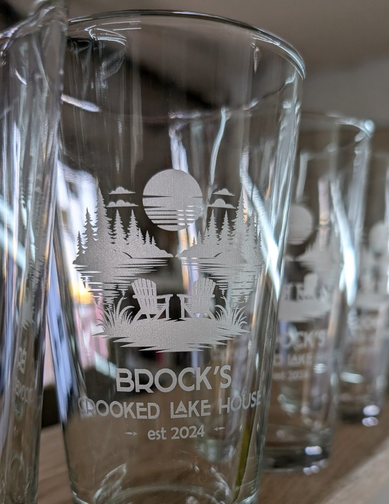 Pint glass etched with a lakeside pine scene for Brock&rsquo;s Crooked Lake House
