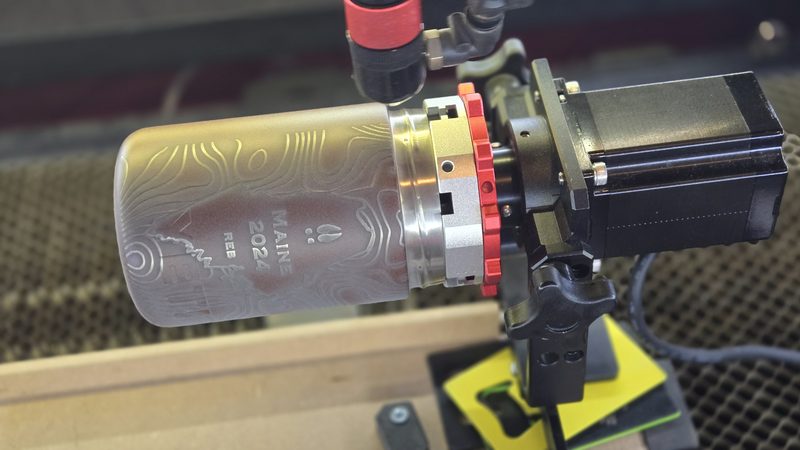 Frosted bottle held in a rotary chuck partway through an etching pass
